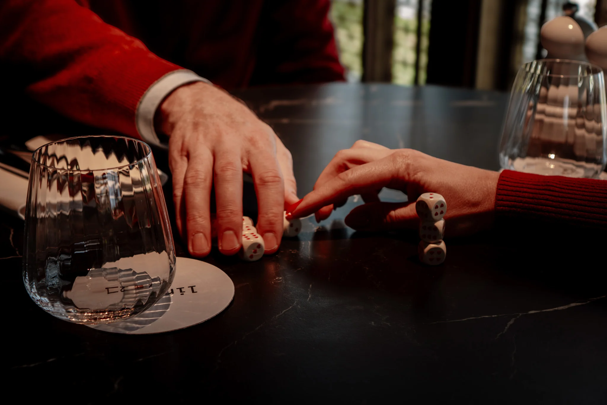 Handen schuiven dobbelstenen over een donkere tafel, detailbeeld uit een videoshoot van Madly